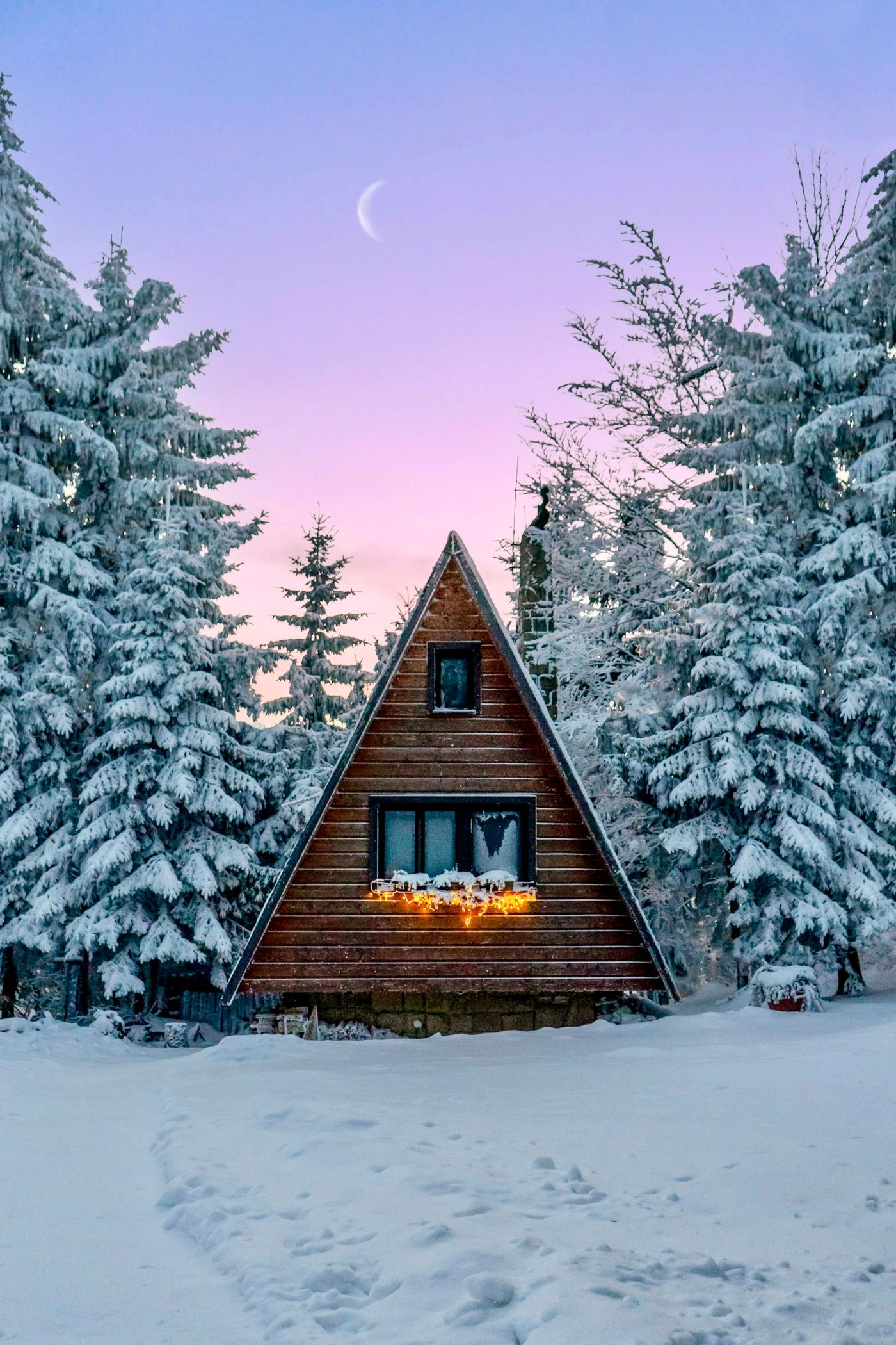 A-frame cabin glowing at twilight among snowy pine trees
