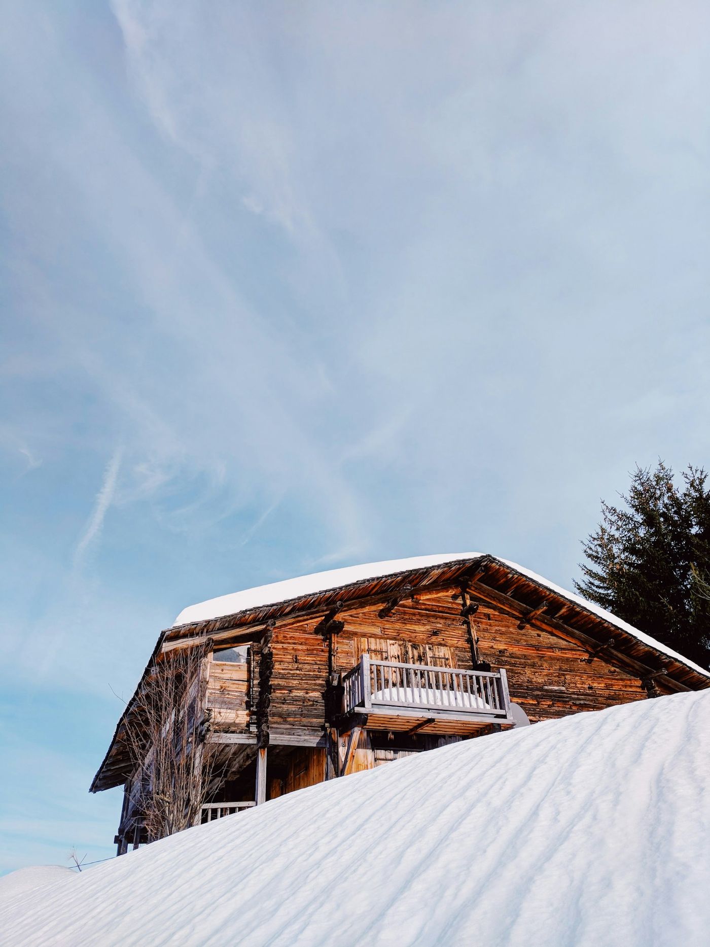 Weathered timber chalet on a sunny snow-covered slope under a blue sky
