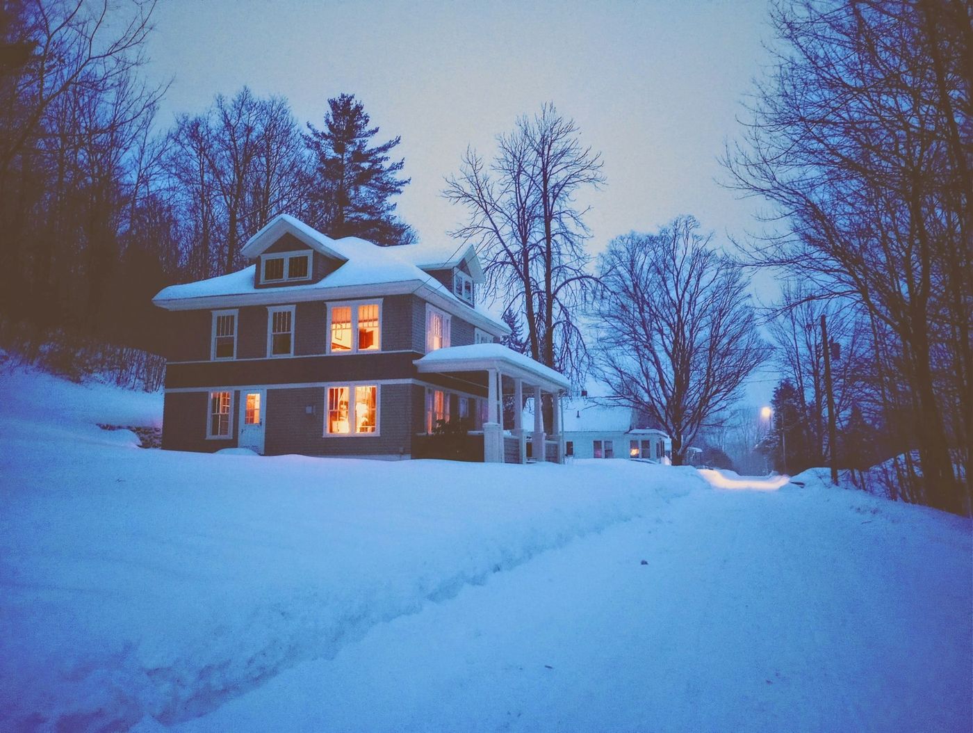 White clapboard house at dusk with warmly lit windows and snow on the ground